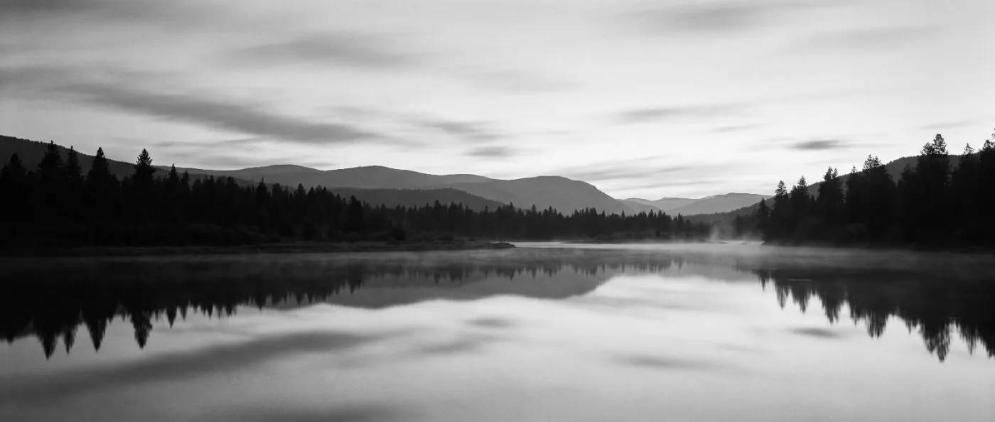 A quiet river bend at dusk, layered hills fading into pale sky